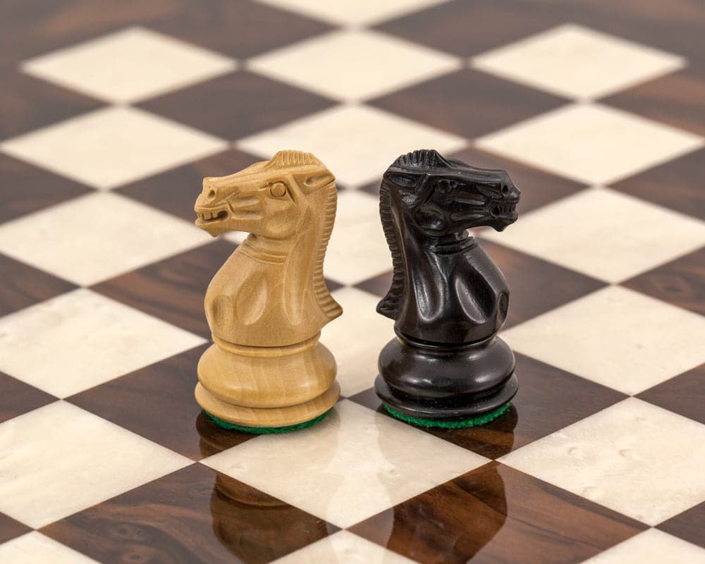 Two carved chess knights on a luxury walnut and maple chessboard with felted bases.